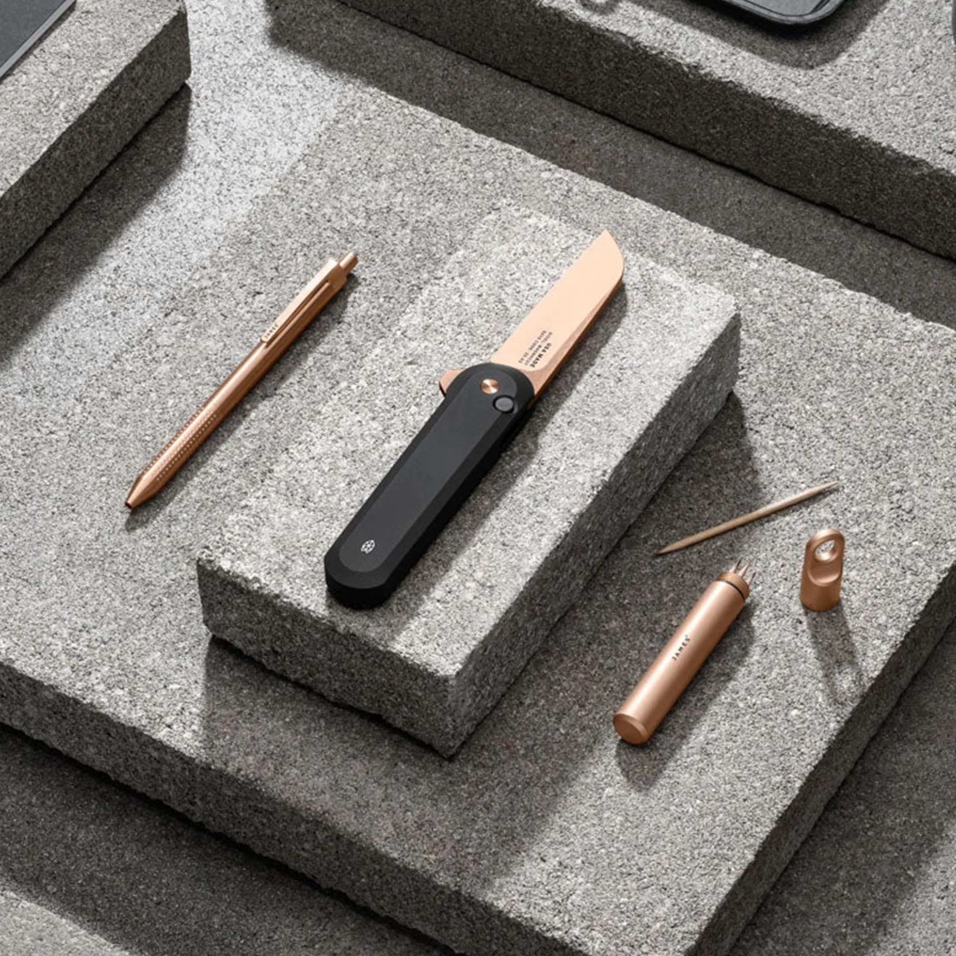 The James Brand Rose Gold Collection knife, pen and capsule sitting on slate blocks