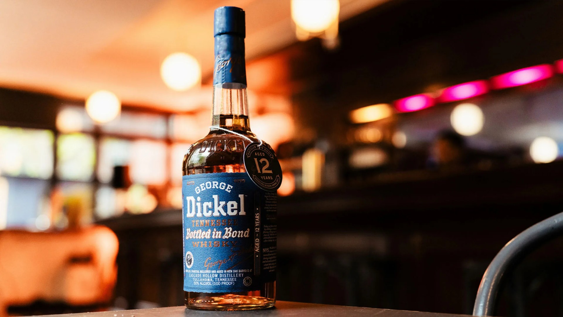 Bottle of George Dickel Bottled in Bond Whisky sitting on table with a blurred dimly lit bar in the background