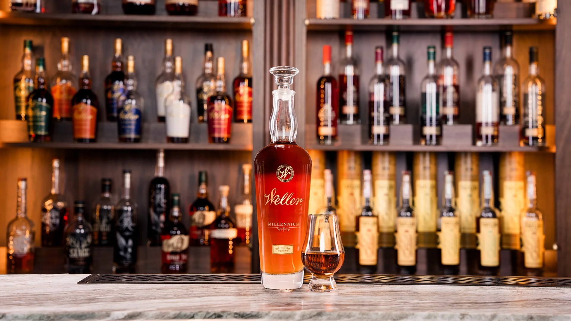 A bottle of W.L. Weller Millenium wheat whiskey sitting on a bar in front of a variety of other whiskey bottles sitting on shelves