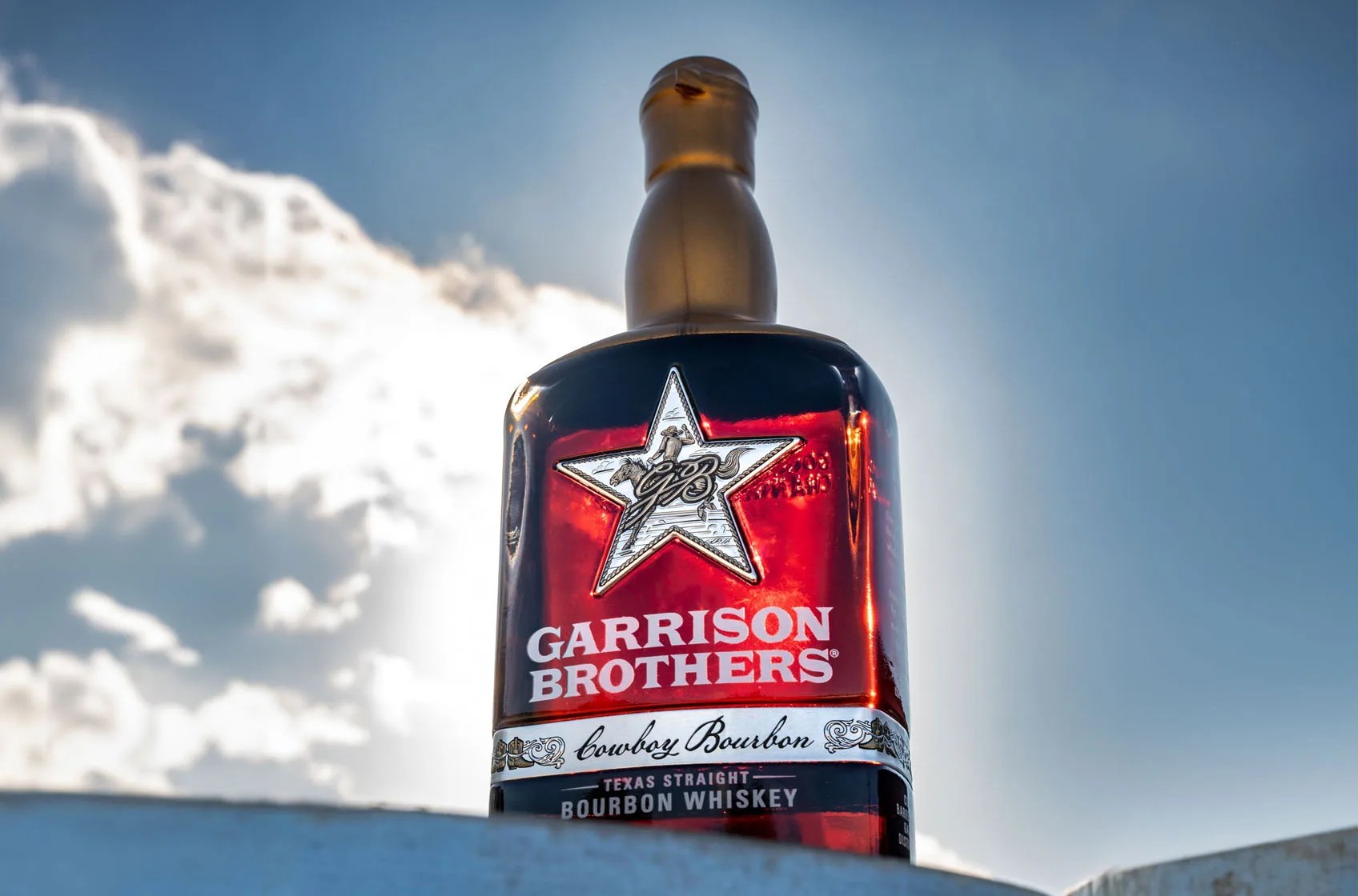 A bottle of Garrison Brothers Cowboy Bourbon 10 Year Anniversary Edition shown with a blue sky background