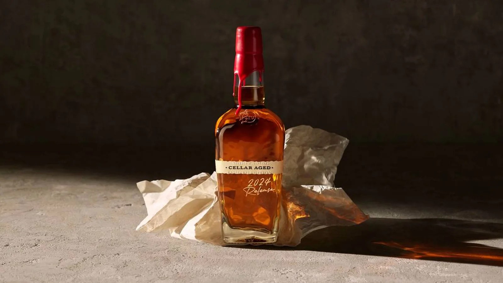 A bottle of Maker's Mark 2024 Cellar Aged bourbon sitting on a piece of crumpled paper lit brightly from the side