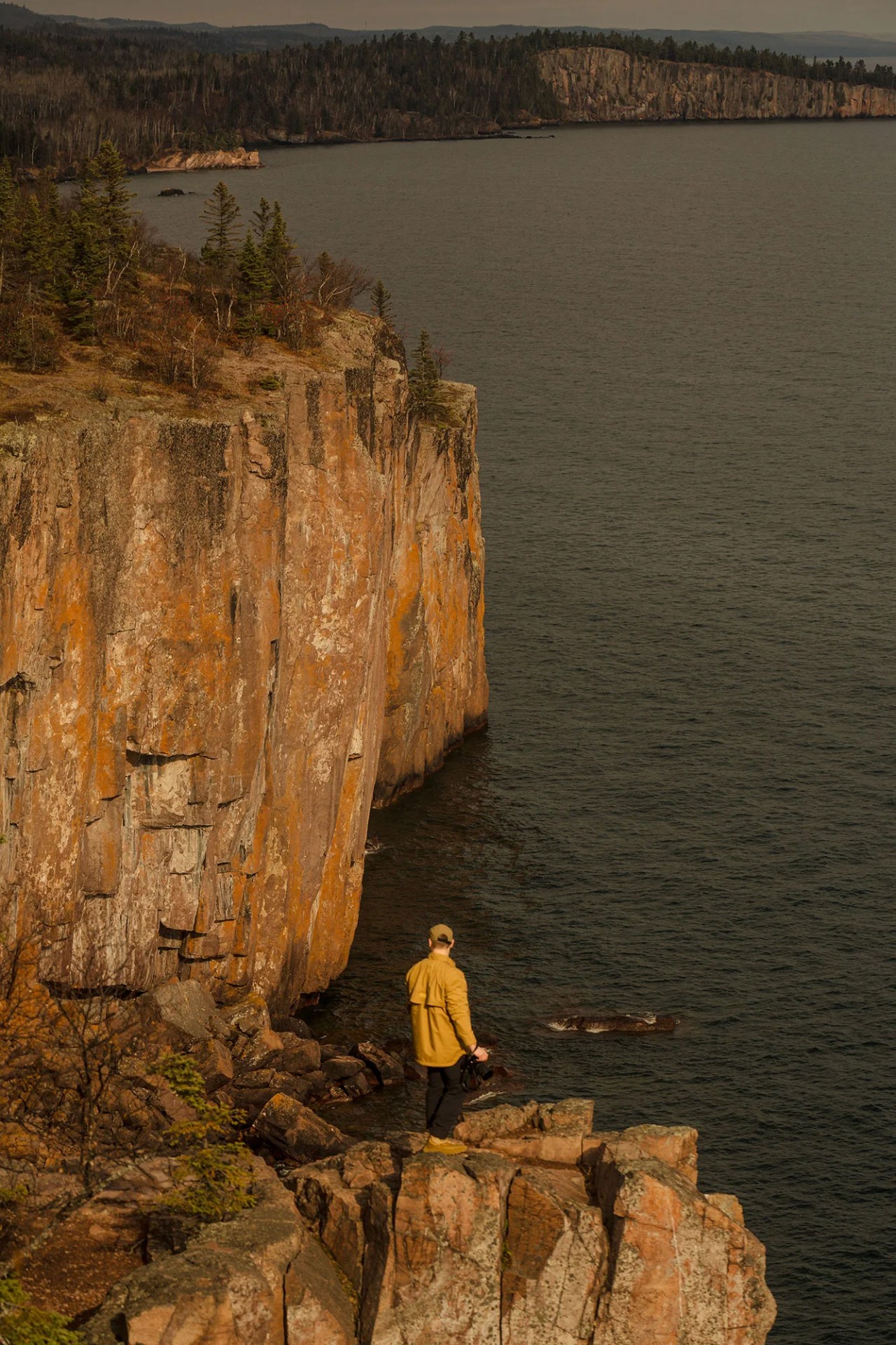 A man peers off a cliff over lake superior